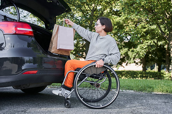 Women in wheelchair loading shopping bags into her car.